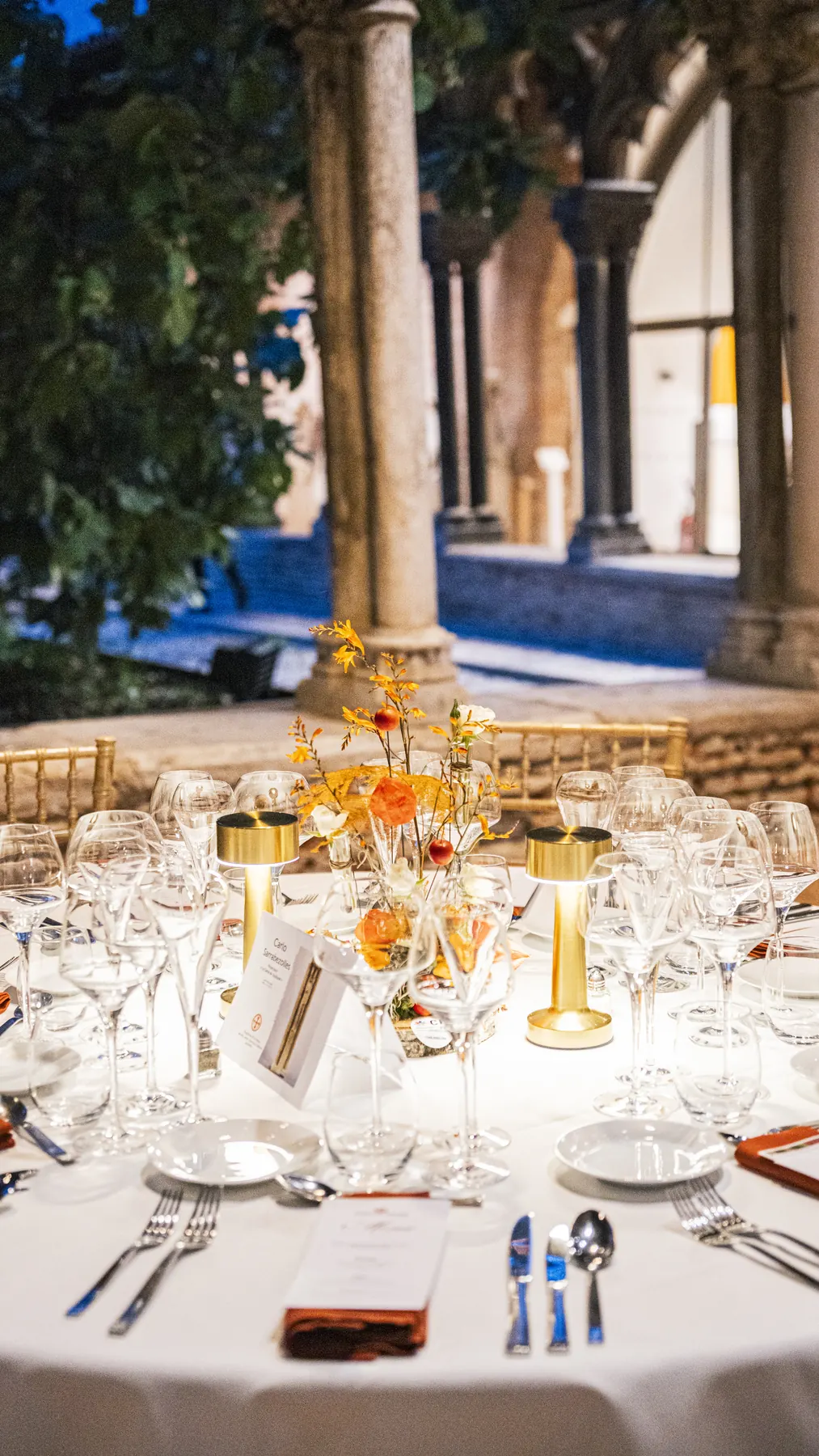 Couvert dressé sous les arcades gothiques du cloître, verrerie et menu